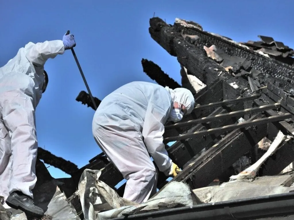 Workers in protective gear clearing debris from a fire-damaged structure.