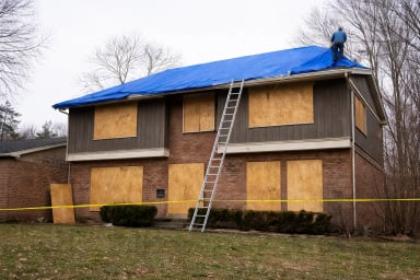 Worker covering damaged roof with blue tarp